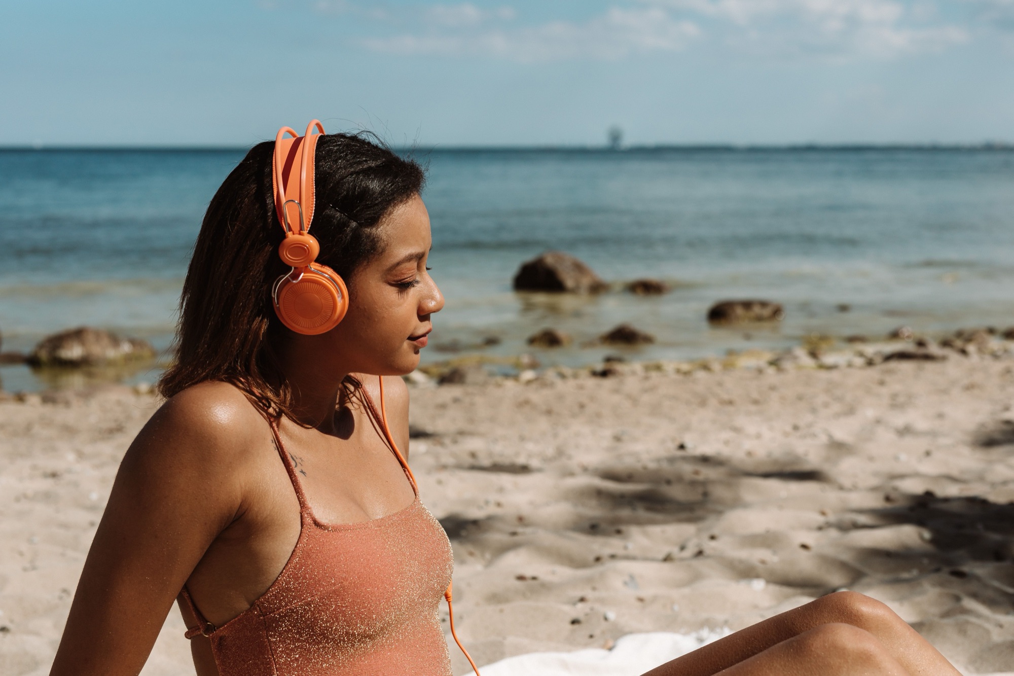 Someone listening with orange headphones on a beach